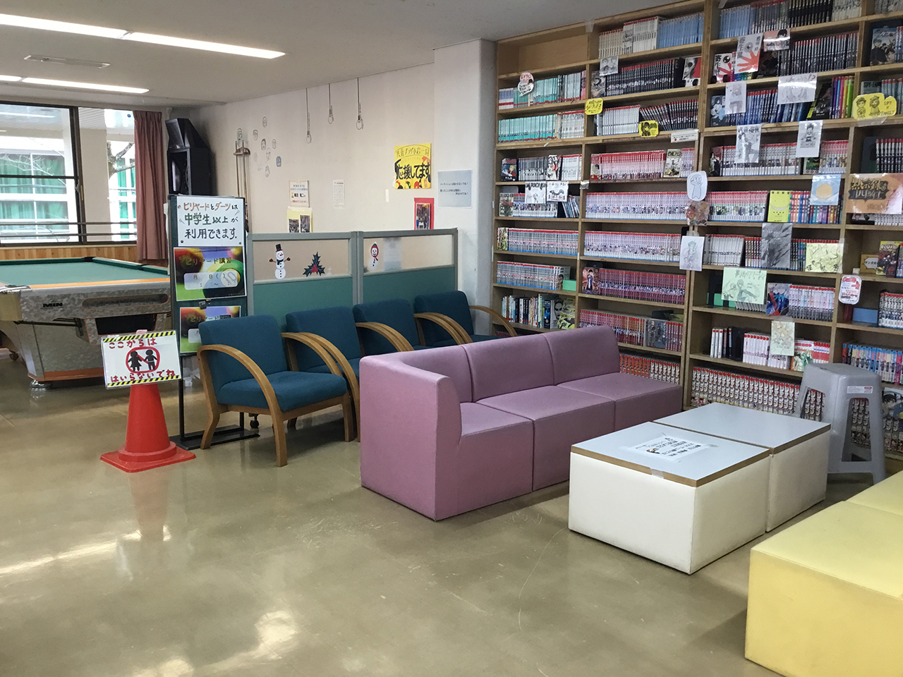 共育プラザ小岩の談話室。テーブル、ソファ、本棚などが見える室内。