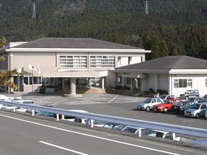 道路の向こう側から見た白い二階建ての施設外観。