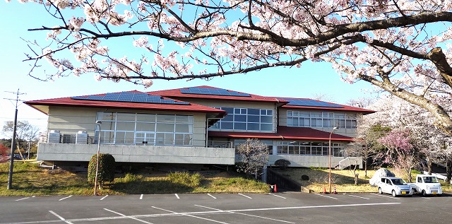 三日月橋生涯学習センターの外観。桜の枝越しに建物と敷地内駐車場が見える。