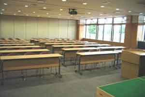 会議室1-A。机と椅子が配置された室内。