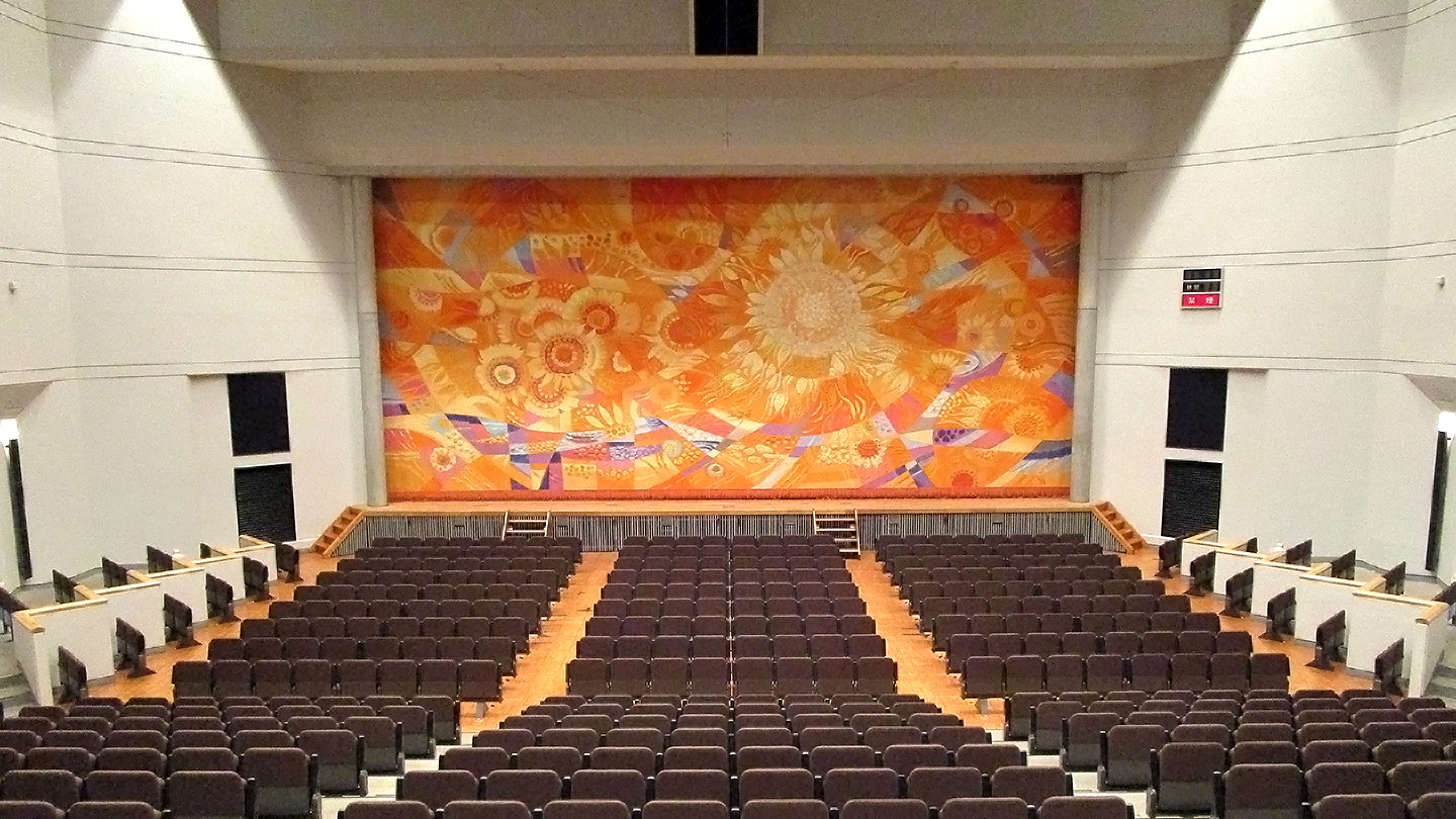 松前総合文化センター 松前町ふるさとライブラリーの客席と舞台、町の花ひまわりを描いた緞帳が見える広域学習ホール。