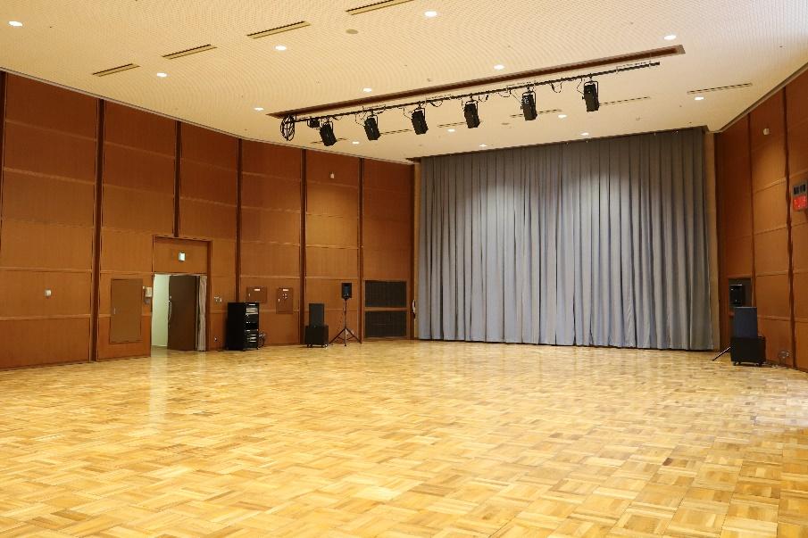 1階の大ホール。ステージカーテンと照明、広い床面が見える。