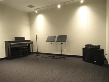 白岡市生涯学習センター（こもれびの森）の音楽スタジオ。ピアノ、マイクスタンド、譜面台、スピーカーがある室内。