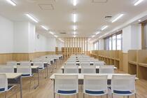 机と椅子が並ぶ学習室と、壁沿いの資料棚が見える。