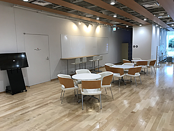 白岡市生涯学習センター（こもれびの森）の木漏れ日広場。丸テーブルと椅子が並ぶスペース。