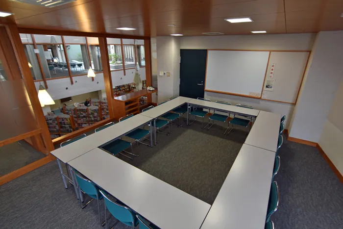 南相馬市民情報交流センター 左奥のガラス越しに中央図書館の開架が見え、ロの字型にテーブルと椅子が置かれた室内の写真