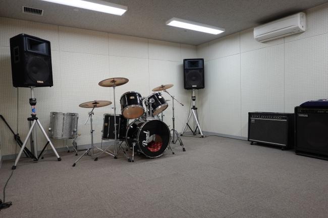 音楽スタジオ。ドラムセットやアンプなどの楽器・音響機材が見える。
