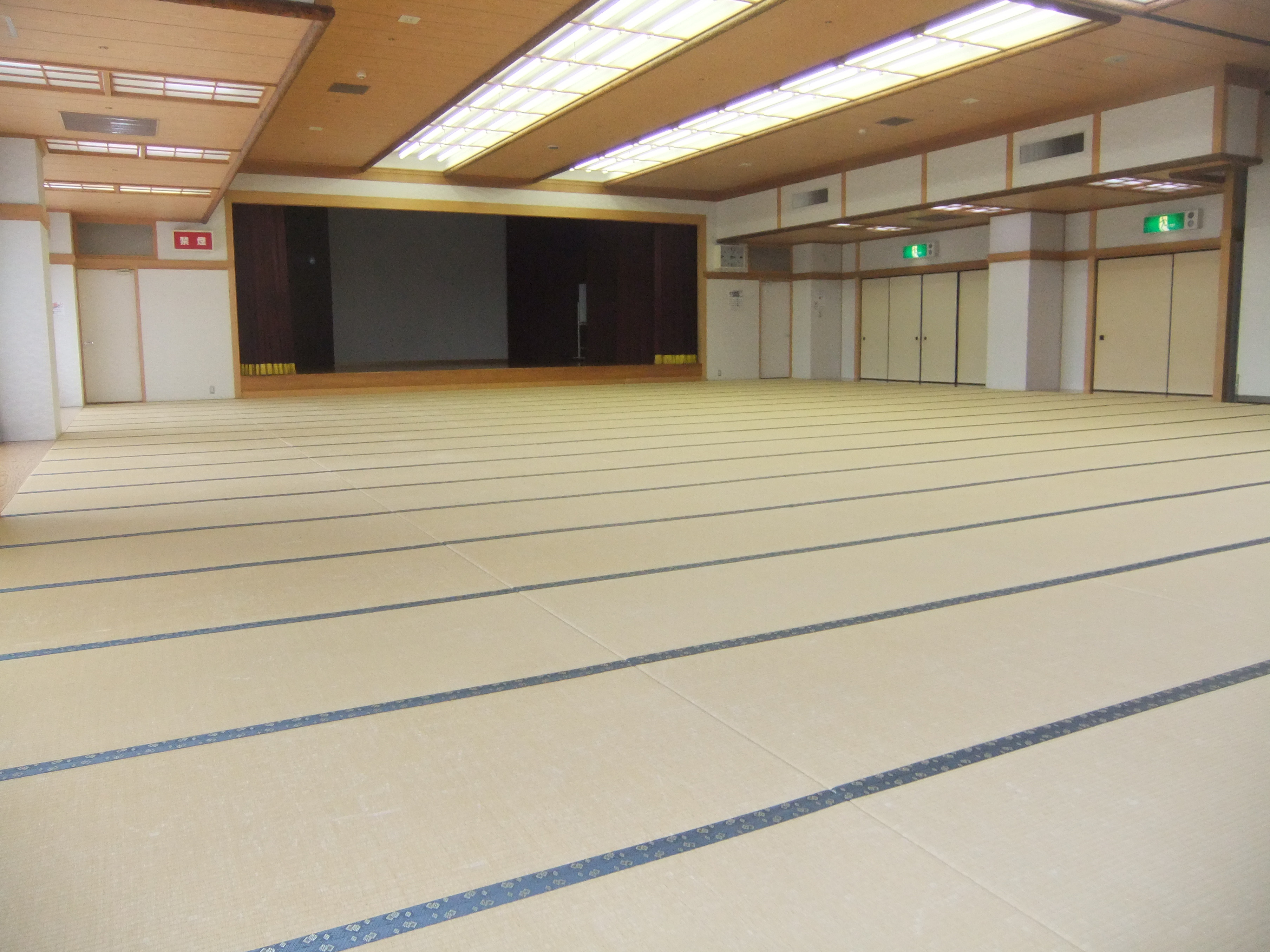 集会室。畳敷きの広い室内に舞台がある。