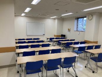 会議室1。青い椅子と机が並び、壁にスクリーンが設置されている。